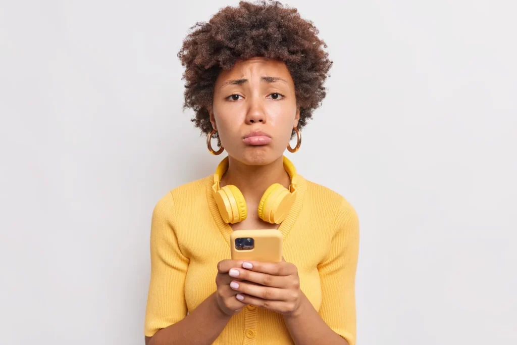 Frustrated woman in a yellow top looking at her phone