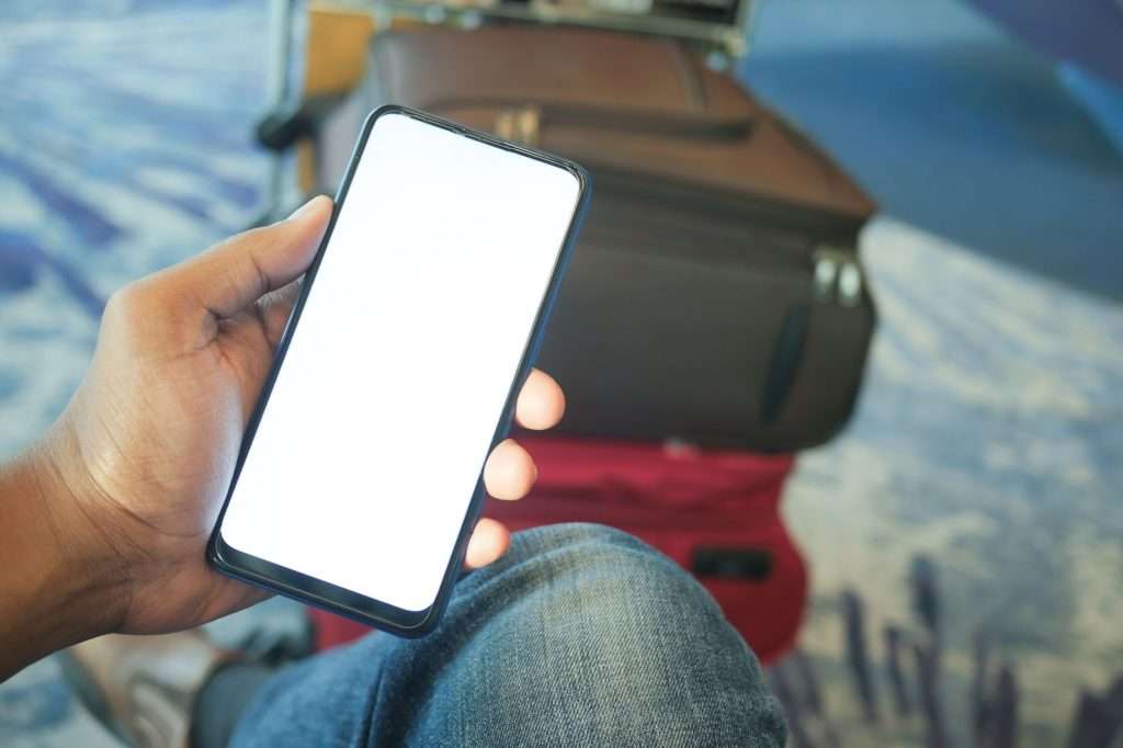 Traveller holding a smartphone beside a suitcase