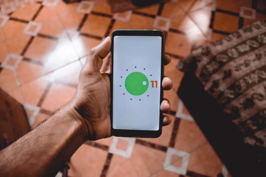 Hand holding an Android phone showing the Android 11 logo