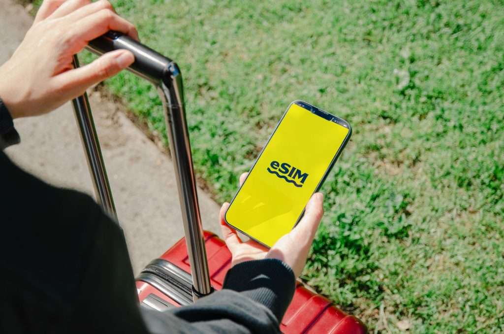 Traveller with a red suitcase holding a phone showing an eSIM screen